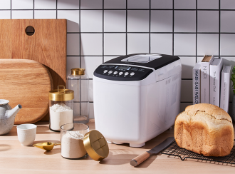 Bread Maker on a kitchen counter top with freshly baked bread on a wire rack along side flour and some cookbooks